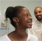 Little girl sits in profile in doctor's office with doctor in background.